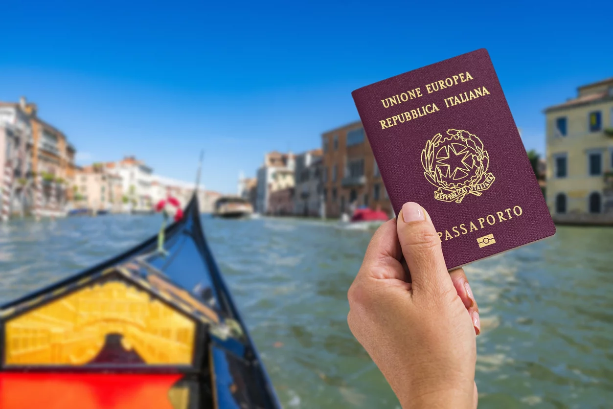 Pessoa segurando passaporte italiano em frente ao canal de Veneza
